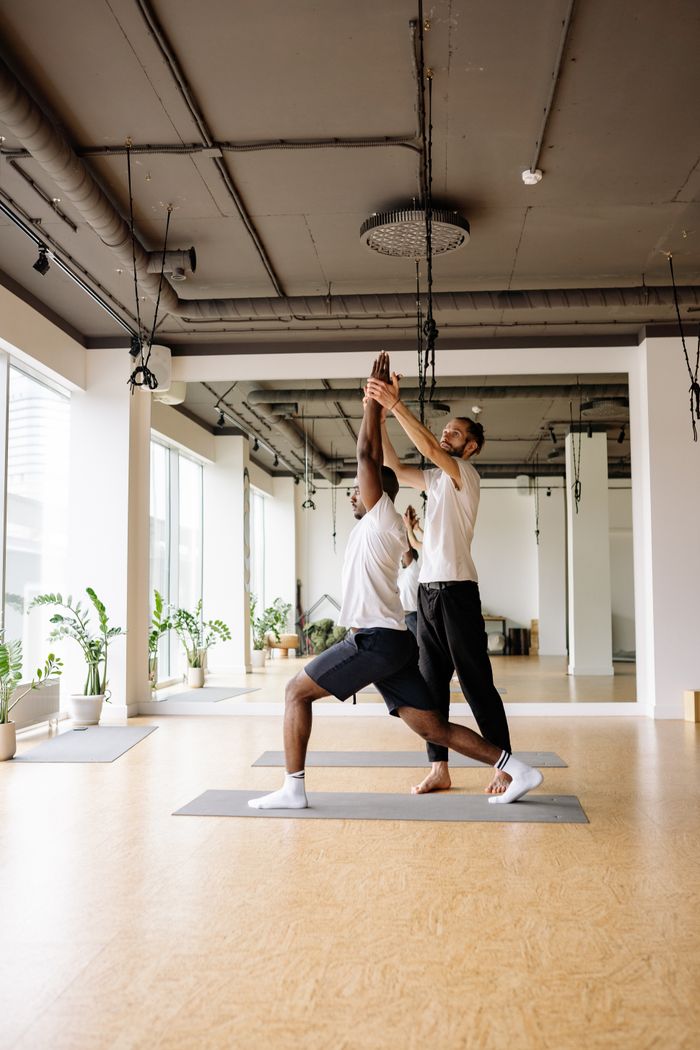 Yoga instructor helps a man stretch in a bright, modern studio.